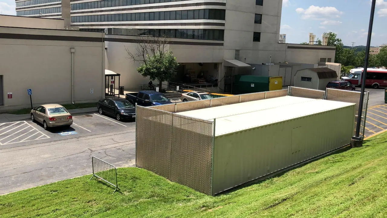 Beige shipping container screened behind a chain-link fence at a commercial property