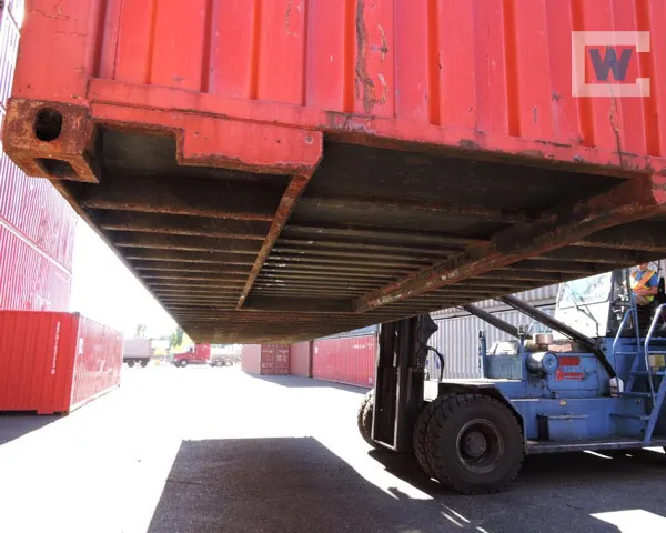 Underside of a shipping container showing steel floor crossmembers on a forklift