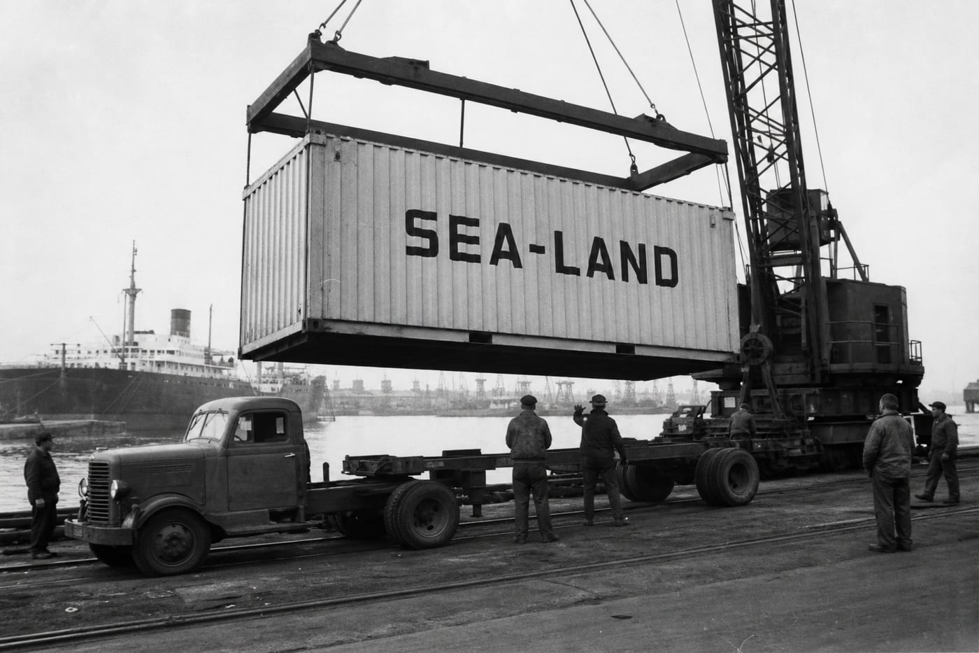 A Sea-Land container being lifted by crane over a truck at a 1950s port.